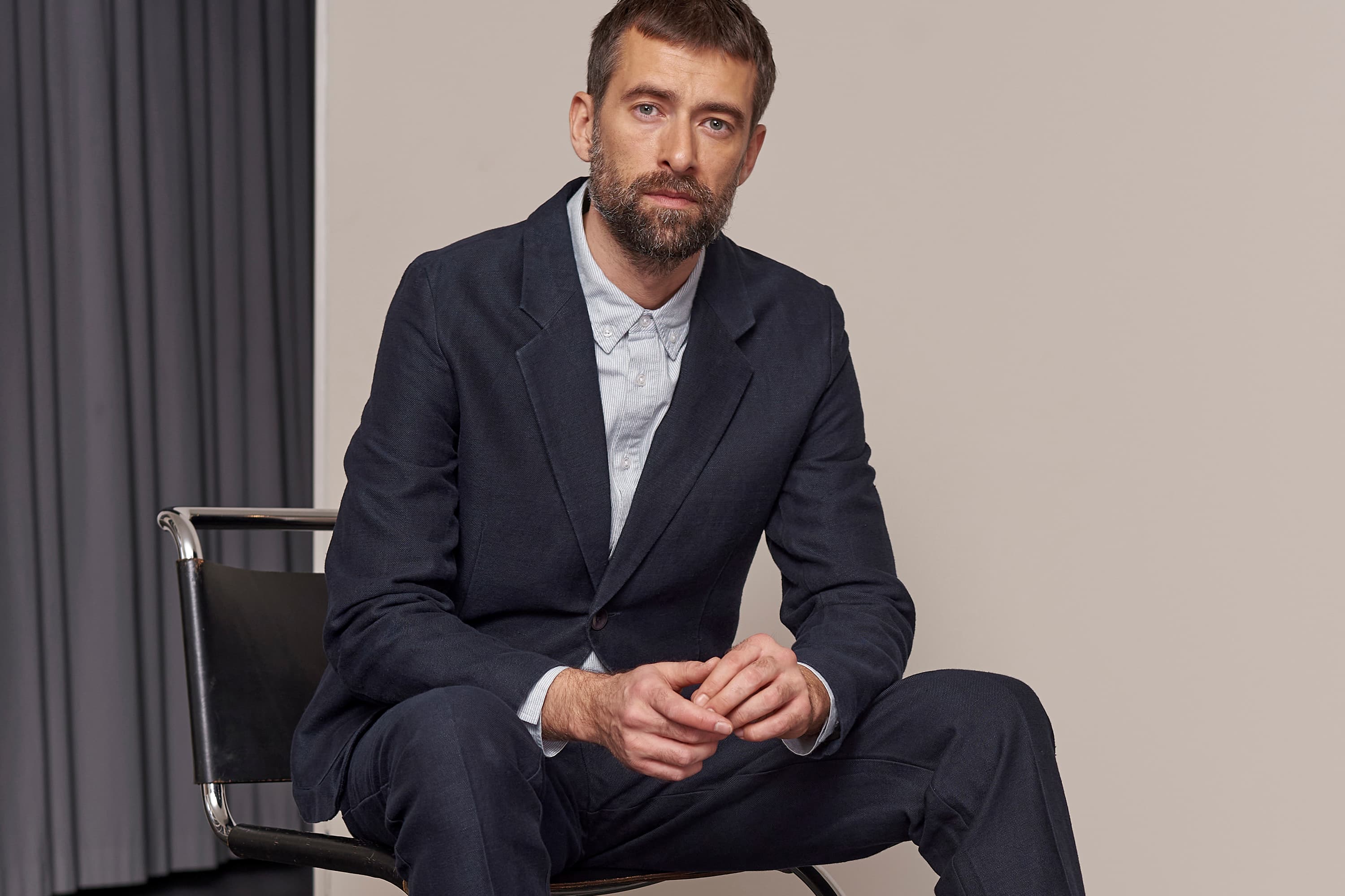 Man sitting in light blue shirt and navy blue suit, facing the camera