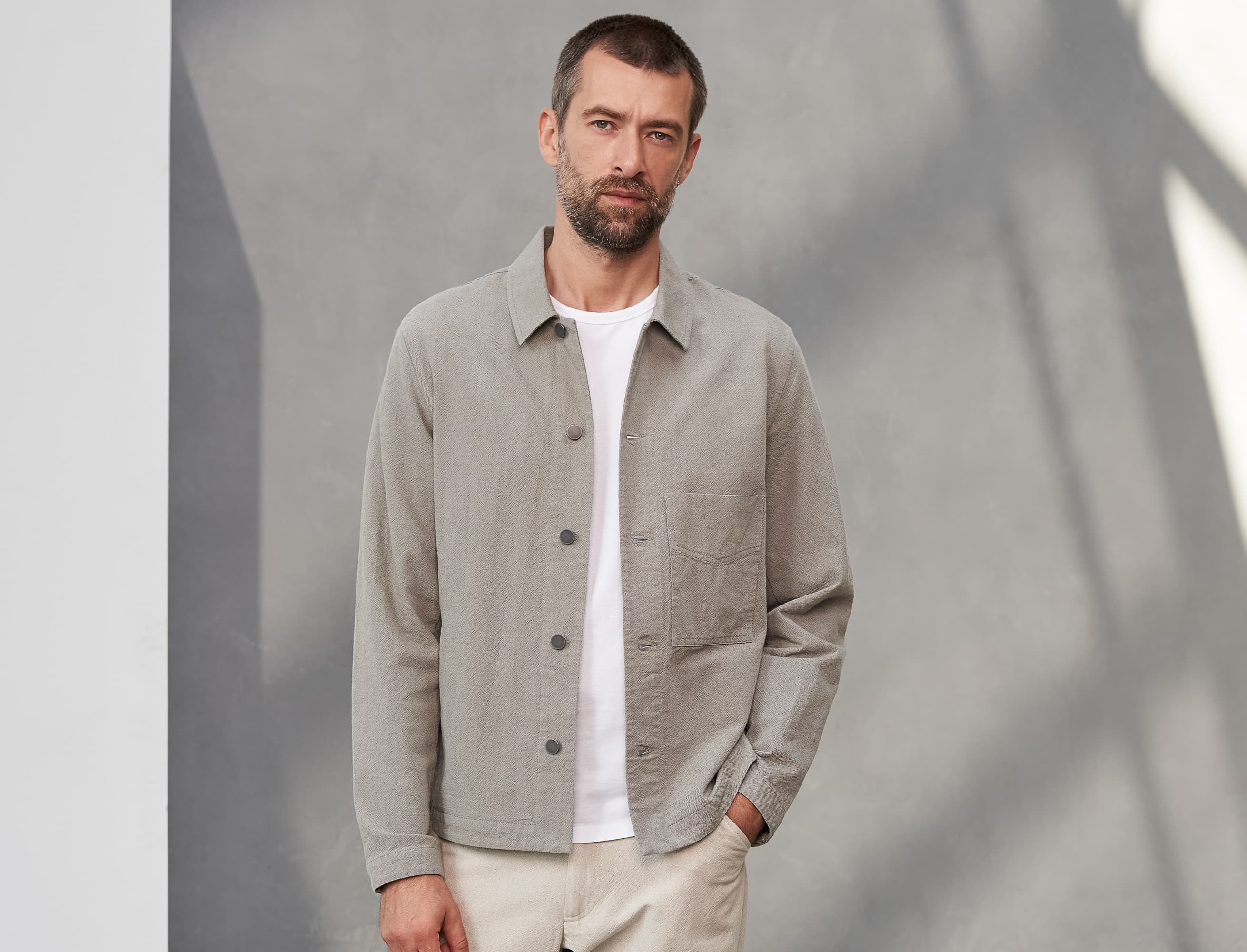 Man wearing a light gray ASIR jacket from About Companions over a white shirt against a neutral background